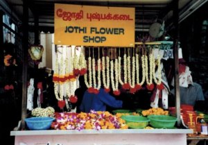 Yellow sign that says Johti Flower Shop With flower necklaces below, located in Singapore