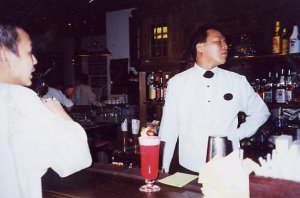 Man in white coat standing behind bar with large red drink in front of him