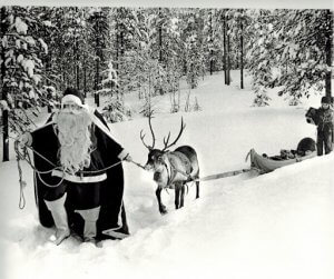 Black and white image of Santa guiding reindeer through snowy forest.